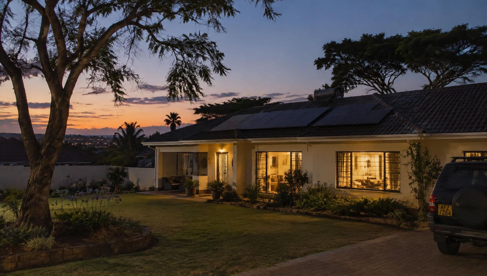 Harare home with rooftop solar panels, lights on at dusk